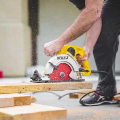 man in black sweatpants using DEWALT circular saw and cutting a wood plank