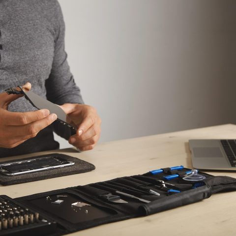 Een kapotte laptop op een werkbank naast een set reparatietools